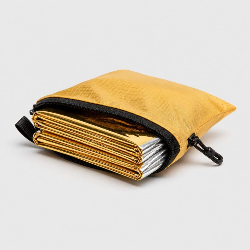 Couverture de survie dorée et argentée repliée dans une pochette compacte
