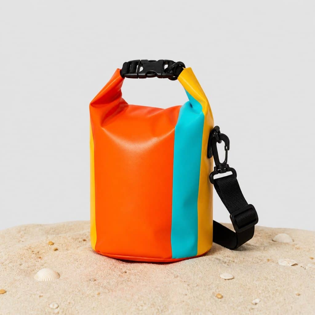Petit sac étanche coloré posé sur le sable d'une plage